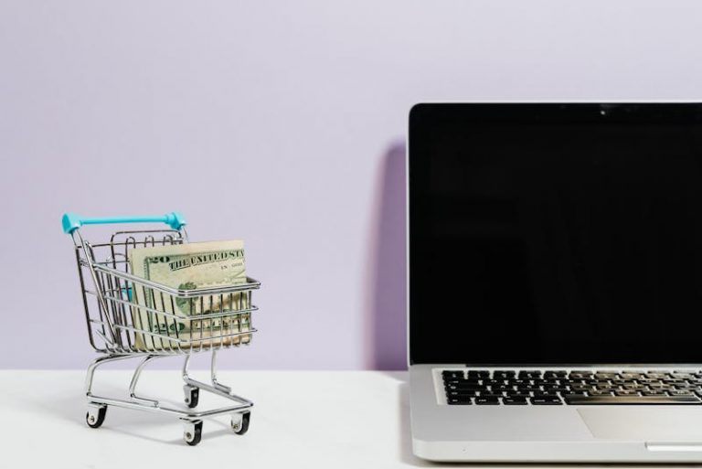 a laptop and a small shopping cart with cash