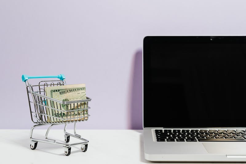 a laptop and a small shopping cart with cash